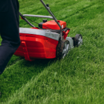 man pushing a red lawnmower on grass,